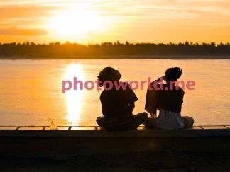 The couple sits on the rocky banks of the Mekong River, Phnom Penh, Cambodia. In love on the river bank. The evening sky is watched by lovers. 01.12.2009