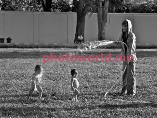 A woman bathes children. Mom waters from the hose of her young children. Children laugh happily and try to dodge the jets of water. December 1, 2009, Mother and children. Phnom Penh, lawn, central square